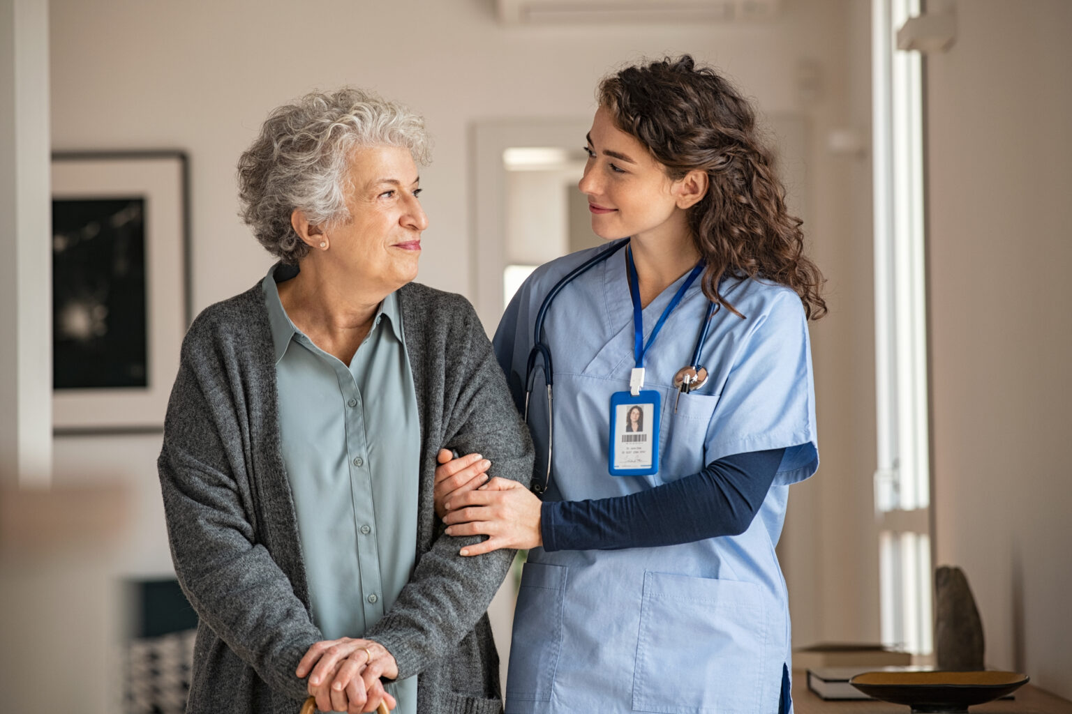 Young caregiver helping senior woman walking. Nurse assisting her old woman patient at nursing home. Senior woman with walking stick being helped by nurse at home.